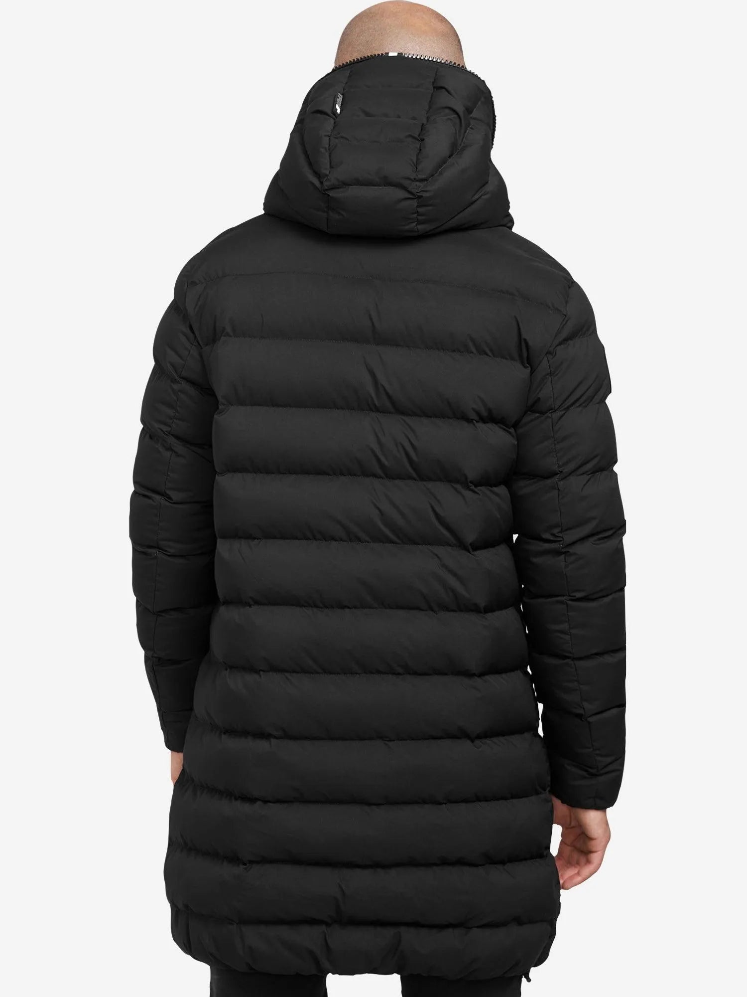 Eine Person trägt eine lange, schwarze Chester Lange Pufferjacke mit Logo von trueprodigy. Der wasserabweisende Herrenparka hat horizontale Nähte und eine Kapuze, die bis knapp über die Knie reicht. Der dezente Reißverschluss unterstreicht das schlichte Design vor einem schlichten weißen Hintergrund.