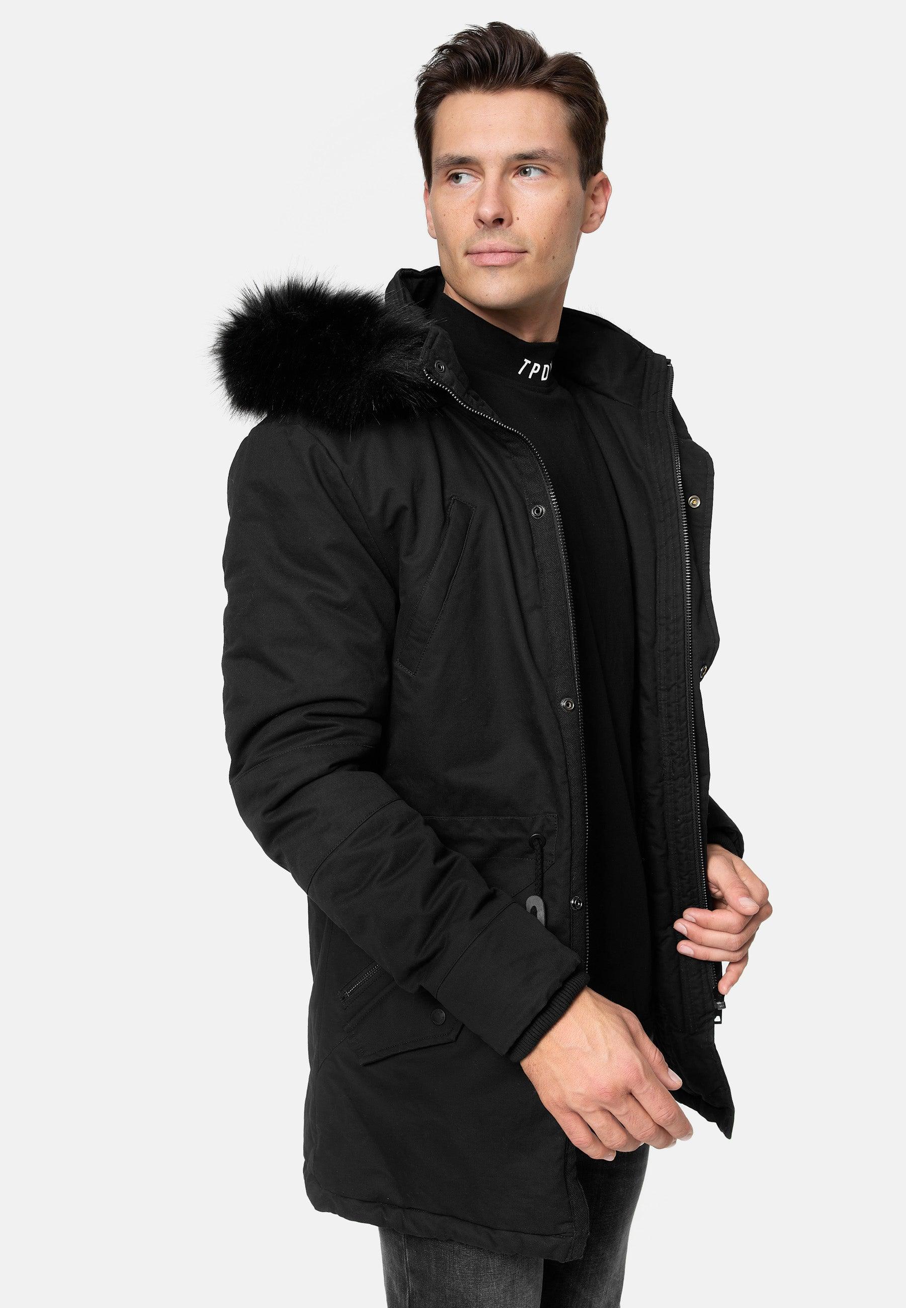 Mann trägt schwarze TRUEPRODIGY julius Winterjacke mit Kunstfellkapuze. Design: minimalistischer Stil, sichtbare Reißverschlüsse. Text auf Rollkragen: TPDY. Ideal für kalte Tage, modisch und funktional.