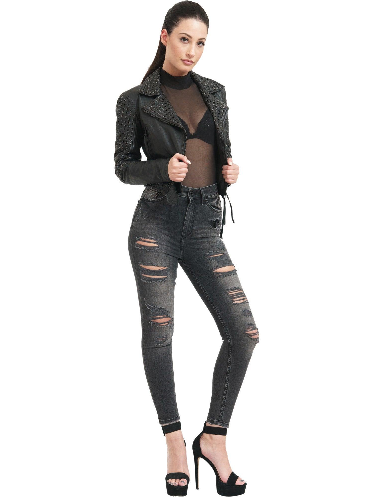 Selbstbewusst gekleidet in einer Raven Bikerlederjacke mit Ösen von trueprodigy, dazu einem transparenten Top und hoch taillierten zerrissenen Jeans posieren sie mit einer Hand auf der Jacke. Schwarze High-Heel-Sandalen vervollständigen den Look vor einem schlichten weißen Hintergrund.